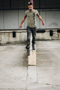 man stepping off ledge wearing an olive graphic tee
