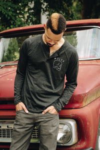 man wearing a black henley leaning on an old vintage truck