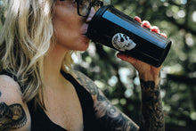 tattooed woman drinking out of a black travel mug with skull design
