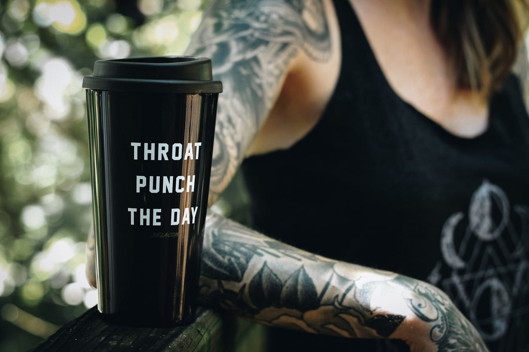 tattooed woman sitting outside with a black travel mug that says throat punch the day