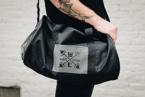 man with tattooed arm holding a small athletic duffle bag