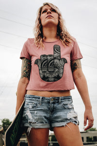 Woman wearing a mauve crop top with a hamsa design and holding a skateboard