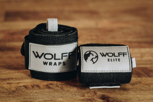 black wrist wraps with wolf logo laying on a hardwood floor