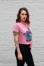 tattooed woman wearing a mauve crop top tee with a hamsa graphic