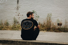 man sitting with black tee and large back graphic design with skulls
